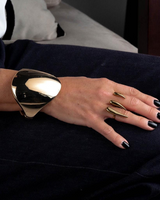 Gold geometric cuff bracelet worn on a wrist, featuring a smooth, bold design with an exaggerated shape.
