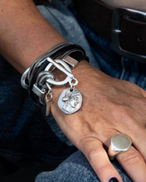Close-up of a hand wearing multiple silver bracelets and rings on a denim background