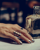 Funky silver-plated metal ring worn among stacked bracelets on a hand with metallic nail polish, resting on a table.