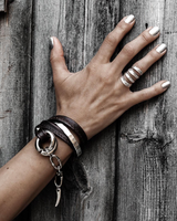Funky silver-plated metal ring worn on the index finger, paired with layered leather bracelets against a wooden background.
