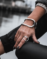 Person wearing silver bracelets and rings with a blurred water background