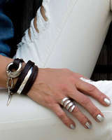 Funky silver-plated metal ring displayed on a hand with silver nail polish, layered with leather and metal bracelets.