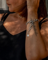 Thick stainless steel chain anklet worn as a bracelet, featuring oval links and a charm, styled with a black top.