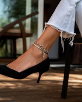 Stainless steel thick chain anklet worn on an ankle, featuring oval links and a charm, paired with a black stiletto.