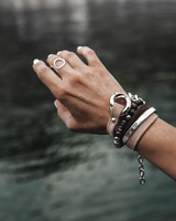 Silver-plated hammered metal bangle stacked with leather and beaded bracelets, worn on a hand.