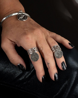 Hand wearing multiple silver rings with dark nail polish on a black background
