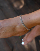 Dainty 999 silver antique plated anklet with round charms, worn on a tanned ankle against a wooden background.