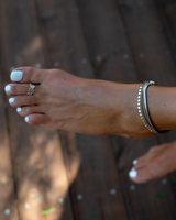 Dainty anklet in antique plated silver with round charms, worn on a bare foot with white toenail polish.