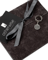 Silver pendant with a gray ribbon on a dark gray surface, branded as 'otherwise jewelry'.