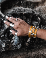 Yellow leather wrap bracelet with a bold buckle, stacked with a matching bangle, worn on a hand against textured rock.
