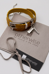 Bright yellow leather wrap bracelet with a bold buckle, stacked with an adjustable bangle on a suede pouch.