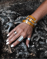 Yellow leather wrap bracelet stacked with a silver bangle, worn on a woman's wrist against a textured rock background.