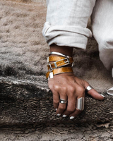 Yellow leather wrap bracelet with bold buckle, stacked with a silver bangle, worn on a casual white outfit.