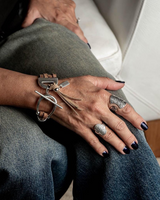 Close-up of a person's hand wearing multiple silver rings and a bracelet on a gray surface.
