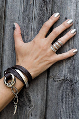 Hand wearing multiple bracelets and rings on a wooden surface