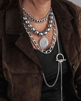 Layered stainless steel chain and gemstone necklace set worn over a black top, showcasing bold silver links and dark beads.
