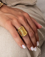 Hand wearing a gold ring with a textured design on a neutral background