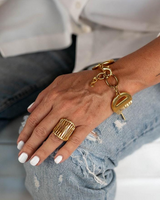 Hand wearing gold bracelet and ring with denim jeans and white shirt in background