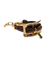 A brown leather wrap bracelet with a gold-tone metal buckle, chain extension, and small rectangular charm, photographed on a plain white background.