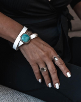 Hand wearing a turquoise stone bracelet and multiple rings on a dark background