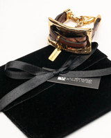 Gold and brown bracelet on a black velvet pillow with a black ribbon, on a white background.