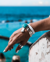 Hand with bracelets and rings against a blurred ocean background