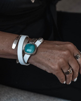 Close-up of a wrist wearing a white leather bracelet with a turquoise stone and a silver ring.