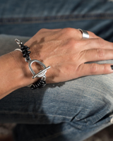 Close-up of a hand wearing a silver bracelet and ring, with denim fabric in the background.