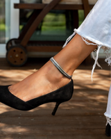 Silver snake chain anklet worn on a bare ankle, paired with a black high-heel shoe, showing its sleek, minimalist design.
