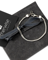 Silver and gun metal snake chain anklet rests on a dark suede pouch, showcasing its sleek, minimalist design.