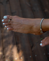 Silver snake chain anklet on an ankle, featuring a charm, paired with a delicate ring on a well-groomed foot.