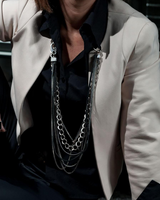 Person wearing a beige blazer and black pants sitting on the ground with jewelry on.