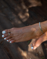 Silver snake chain anklet worn on a bare foot, showcasing a sleek design against a natural wood background.