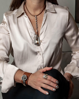 Person wearing a white satin shirt with jewelry, including a necklace, watch, and rings.