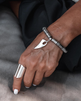 Hand wearing a silver ring and bracelet on a textured surface
