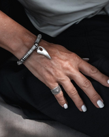 Close-up of a hand wearing a silver bracelet and ring on a dark background