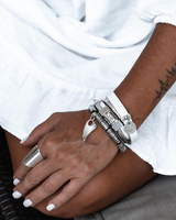 Close-up of a person's arm with silver bracelets and a ring, wearing a white shirt.