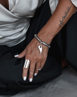 Person wearing a silver ring and bracelet with a pendant, sitting on a gray surface.