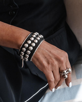 Close-up of a hand wearing a black leather bracelet with silver studs and multiple rings.
