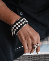 Hand wearing a studded bracelet and ring, holding a clutch with a blurred background