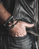 Hand wearing a leather glove with a bracelet, holding a gun, against a dark background.