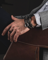Person wearing a gray suit with a brown leather jacket, sitting on a dark chair.