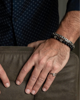 Close-up of a person's hands on a leather surface, wearing watches and rings.