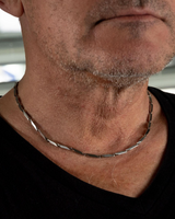 Close-up of a person wearing a silver chain necklace with a blurred background