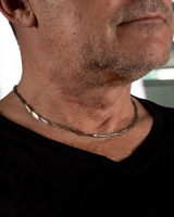 Close-up of a man wearing a silver necklace with a blurred background