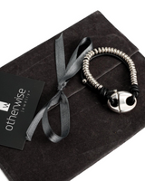 Silver bracelet with black accents on a dark fabric surface with 'otherwise jewelry' card.