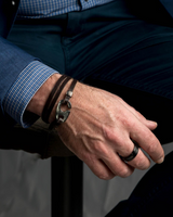 Person wearing a bracelet and ring, sitting with crossed legs on a dark surface.