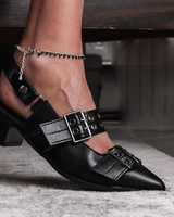 Black pointed-toe shoes with buckles worn by a person on a blurred background