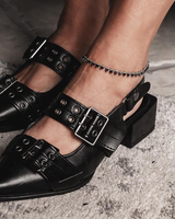 Black pointed-toe shoes with buckles worn by a person on a concrete surface
