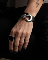 Hand wearing a silver bracelet and black ring with a blurred background